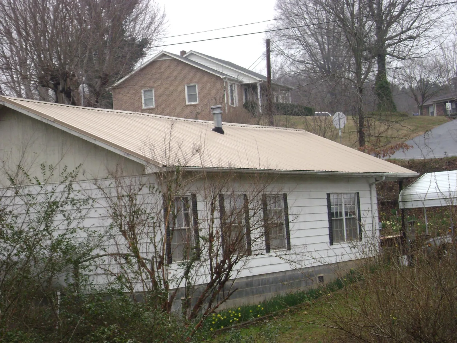 Tan metal roof on a white sided house set into a hillside — Commercial Roofing by Roofing Brothers in Croydon