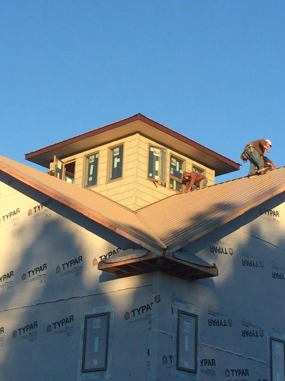 Roofers working around a rooftop cupola on a new metal roof at sunset — Roof Waterproofing in Croydon by Roofing Brothers
